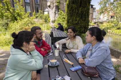 Four students drinking coffee around a picnic bench