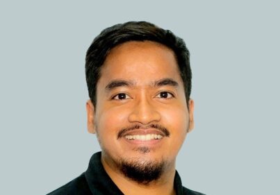 Smiling man with short black hair wearing a black polo shirt against a light gray background, portrait-style photo.